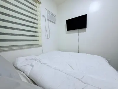 a white bed in a bedroom with a television on the wall at Urban Deca Towers Cubao in Manila