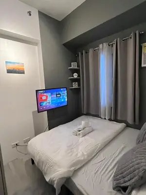 a bedroom with a bed with a flat screen tv at Cozy Makati 2BR in CBD Ayala area with games, KTV, and Amazing Pools! in Manila