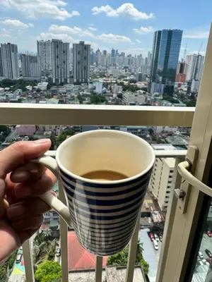 a person holding a cup of coffee on a balcony at Coast Residences Ivy in Manila