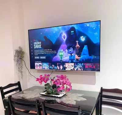 a television hanging on a wall with a table with flowers at 352B Shell Residences Barkada Room in Manila