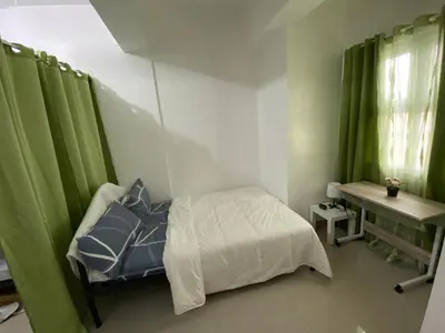 a bedroom with a bed and a desk and green curtains at Gen coZy Condo Stay by Victoria de Manila Tower in Manila