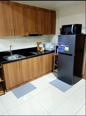 a kitchen with a black refrigerator and wooden cabinets at Len's Den 3 Entire Flat in Mall of Asia Pasay Manila in Manila