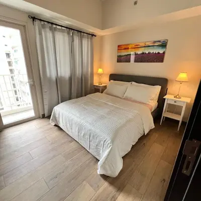 a bedroom with a large bed and two tables with lamps at A1 Suite in McKinley in Manila