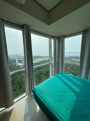 a bedroom with large windows and a bed with blue sheets at Breeze Deluxe Unit Roxas blvd in Manila