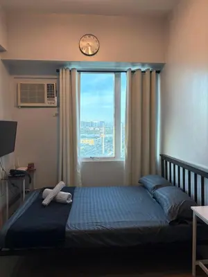 a bedroom with a bed and a window with a clock at Anuva Condo Staycation in Manila