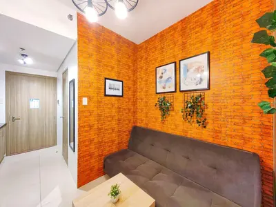 a living room with a couch against a brick wall at 1BR Condotel with Balcony at FAME Residences #FM04-1 in Manila