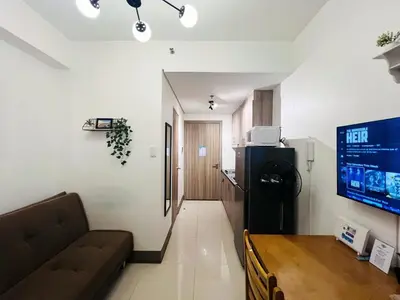 a living room with a couch and a refrigerator and a television at 1BR Condotel with Balcony at FAME Residences #FM12-1 in Manila