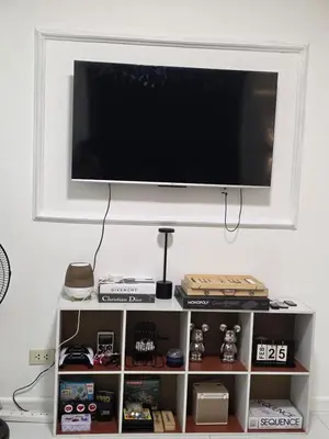 a tv on a wall above a shelf with games at Casa Serenity Staycation at Azure parañaque with 1 bedroom good for 1 to 4 pax airconditioned room and pool view near sm bicutan in Manila