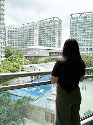 a woman looking out of a window at a pool at Casa Serenity Staycation at Azure parañaque with 1 bedroom good for 1 to 4 pax airconditioned room and pool view near sm bicutan in Manila