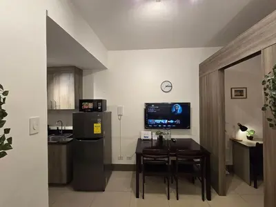 a kitchen with a table and a television in a room at 1BR Condotel with Balcony at FAME Residences #FM21-1 in Manila