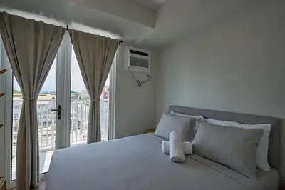 a bedroom with a white bed with a large window at I-LAND Residences Sucat near NAIA w Wifi free parking in Manila