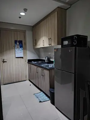 a kitchen with a black refrigerator and wooden cabinets at Zenys Staycation at Shore 1 Residences in Manila