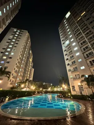 a large pool in between two tall buildings at night at Cozy Condo at South Residences in Manila
