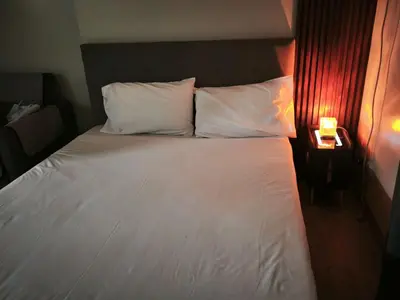 a bed with white pillows and a night stand with a lamp at Modern Studio Condo in Heart of Quezon City in Manila