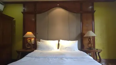 a bed with a wooden head board and two lamps at Hassan Sisters' EnSuites in Manila