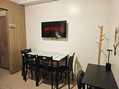 a table with chairs and a television on a wall at Spacious 1BR beside MOA with Wifi, Netflix, Pool & Washer in Manila