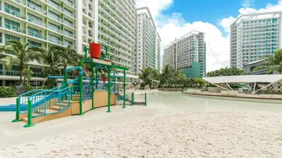 a playground in the middle of a beach with tall buildings at Cozy Green 1 BR unit with Balcony Azure Bahamas South in Manila