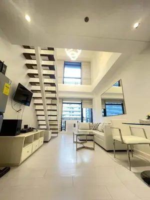 a large living room with white furniture and stairs at Minimalist 1 Bedroom Loft Makati in Gramercy Residences in Manila