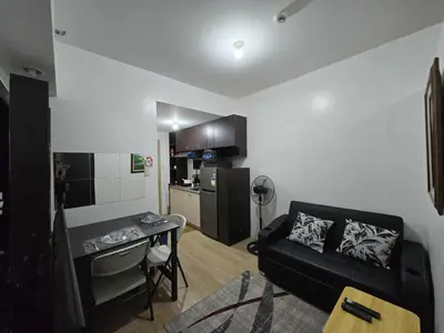 a living room with a black couch and a kitchen at SMDC Shine Residence in Manila
