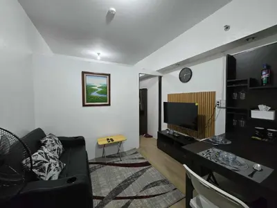 a living room with a black couch and a television at SMDC Shine Residence in Manila
