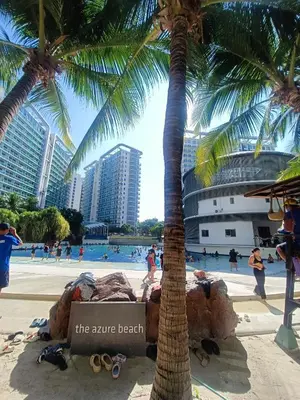 a palm tree on a beach with people in a pool at Azure Urban Resort Staycation in Manila