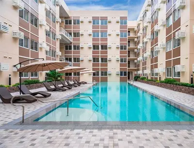 a swimming pool with chairs and an umbrella next to a building at Cozy Studio near Nuvali, Enchanted Kingdom - Private Cinema with Netflix & Disney Plus with Free Pool Access in Silang