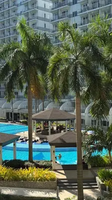 a swimming pool with palm trees in front of a building at Spacious Condo at Shell Residences, MOA Pasay - The Urban Stay in Manila