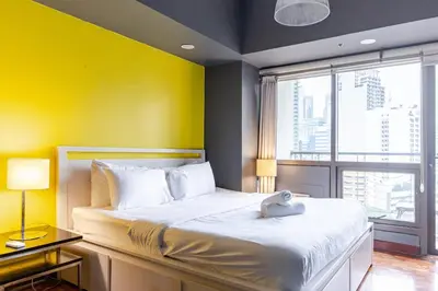 a bedroom with a large bed with a yellow wall at Central Stay w King bed near Greenbelt 55-In TV in Manila