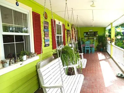 a porch of a green house with two white benches at Madie's Place B&B with Private Pool in Santa Rosa near Enchanted Kingdom in Santa Rosa