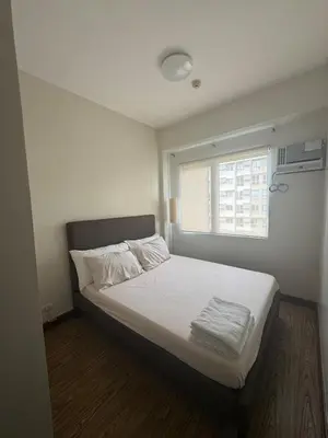 a bedroom with a bed with white sheets and a window at East Bay Residences Condo Unit in Muntinlupa in Manila