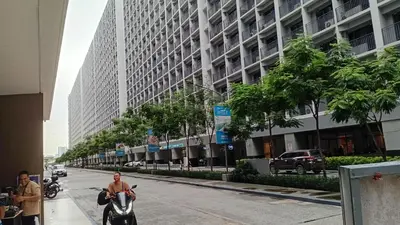 a man riding a scooter down a street with a tall building at Casa Via at Shore 2 Residences inside SM MOA Complex, Pasay City in Manila