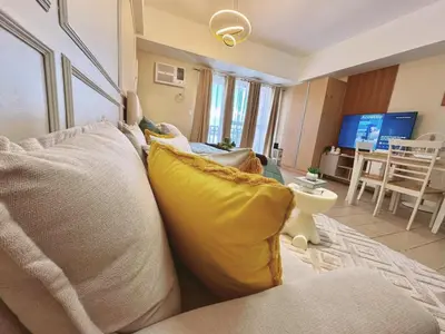 a living room with a couch with yellow pillows at Cozy Unit near Venice Grand Canal Mall McKinley Hill Taguig in Manila
