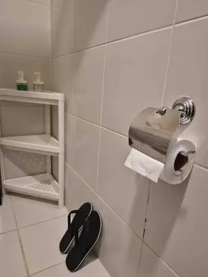 a bathroom with a toilet paper dispenser and a pair of shoes at B&C Studio Kasara Urban Resort Residences in Manila