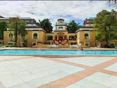 a large yellow building with a pool in front of it at 1BR Cozy Home with Balcony Near NAIA Terminals in Manila