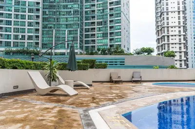 a pool with chairs and an umbrella and some buildings at Julias Upscale Airy Getaway 1 BR Golf View in Manila