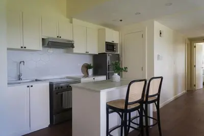 a kitchen with white cabinets and two bar stools at Elegant and Modern 2 BR Home Golf Skyline View in Manila