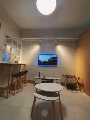 a living room with a table and a tv on the wall at Minimalist Big 1BR Pool View MOA Airport in Manila