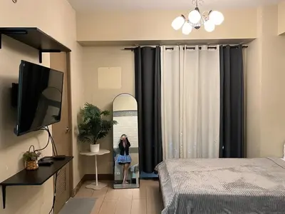 a woman standing in front of a window in a bedroom at Kyendenz Condotel-Across Naia T3 Pool View with Wifi in Manila
