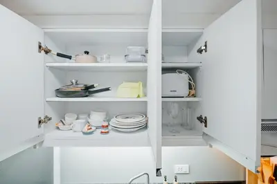 a white pantry with dishes and utensils at Coastal Studio in KL Tower Serviced Residences, Greenbelt, Makati! Maximum capacity 5 pax! in Manila