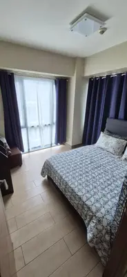 a bedroom with a bed with a blue comforter and windows at Rqui Condotel Pasay City Manila in Manila