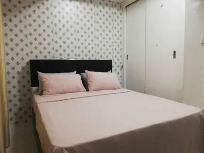 a bedroom with a bed with white sheets and pink pillows at Grand Riviera Condotel Near St lukes Medical Center in Manila