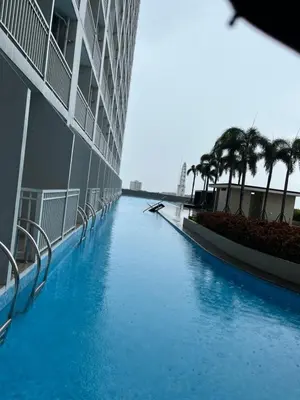 a swimming pool with palm trees in front of a building at Breeze Residences pasay near naia airport in Manila