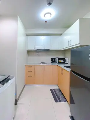 a kitchen with white cabinets and a black refrigerator at 1 BR Cozy unit Uptown Parksuites BGC in Manila