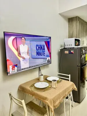 a television on a wall with a table and a refrigerator at Relaxing City Retreat in Manila