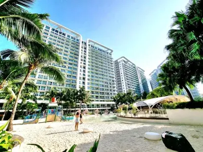 two people standing on the beach in front of a resort at 1BR Unit Azure Urban Resort Residences in Manila