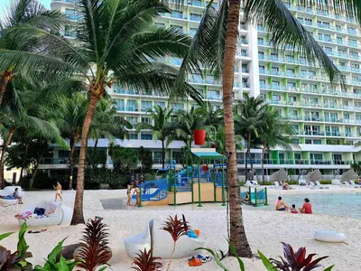 a beach with a playground and palm trees and a large building at 1BR Unit Azure Urban Resort Residences in Manila
