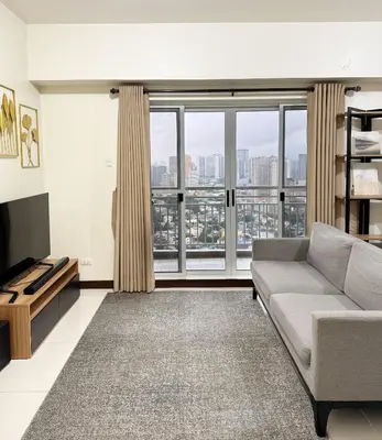 a living room with a couch and a large window at Corner 37 at Lumiere Residences in Manila