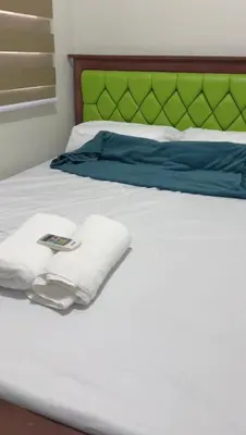 a white bed with a green headboard and towels on it at Transient Room in Dasmariñas