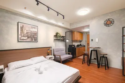 a bedroom with a white bed and a kitchen at SMDC Lush The Forge in Manila