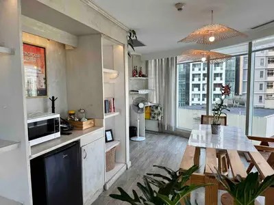 a living room with a table and a kitchen with a window at 55-SQM The Urban Cabin in Poblacion Makati in Manila